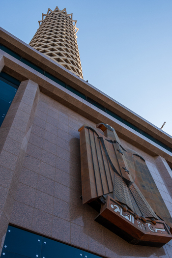 View of a towering Cairo Tower rises beyond a building adorned with an emblem against the backdrop of a clear sky Zamalek Cairo Governorate Egypt. View of a towering Cairo Tower rises beyond a building adorned with an emblem against the backdrop of a clear sky Zamalek Cairo Governorate Egypt.