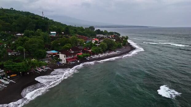 Aerial view of coastal village and black sand beach in Indonesia.