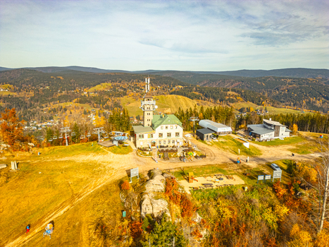 Aerial view of the Tanvaldsky Spicak lookout tower and mountain lodge surrounded by autumn forests and ski slopes in Tanvald Liberecky kraj Czechia.
