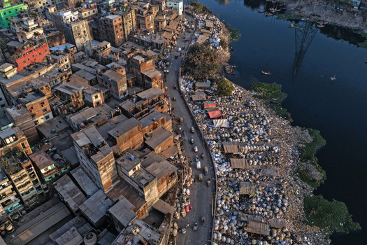 Aerial view of Buriganga River flowing past dense urban buildings and a busy road with traffic in Dhaka Dhaka Division Bangladesh. Aerial view of Buriganga River flowing past dense urban buildings and a busy road with traffic in Dhaka Dhaka Division Bangladesh.