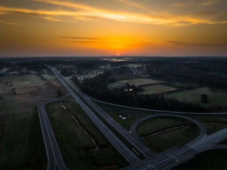Aerial view of the A5 and A8 highway interchange at sunset featuring sweeping roads surrounding fields and a vibrant orange sky in Olaine parish Olaine Municipality Latvia. Aerial view of the A5 and A8 highway interchange at sunset featuring sweeping roads surrounding fields and a vibrant orange sky in Olaine parish Olaine Municipality Latvia.