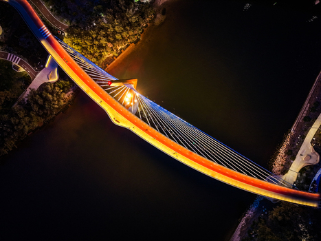 Aerial view of the illuminated Boorloo Bridge spanning the Swan River at night with vibrant orange lighting and modern cable stayed architecture in East Perth Western Australia Australia.