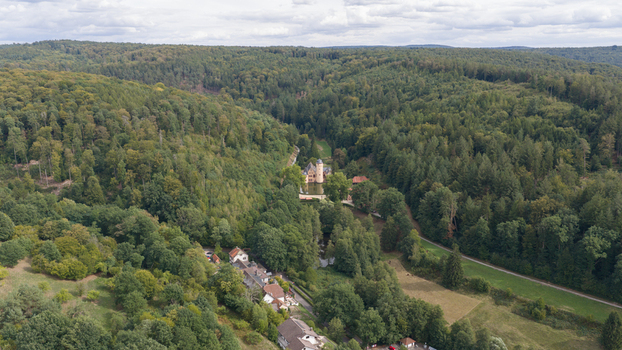Aerial view of Schloss Mespelbrunn nestled in a lush green valley surrounded by dense forest and rolling hills in Mespelbrunn Bayern Germany.