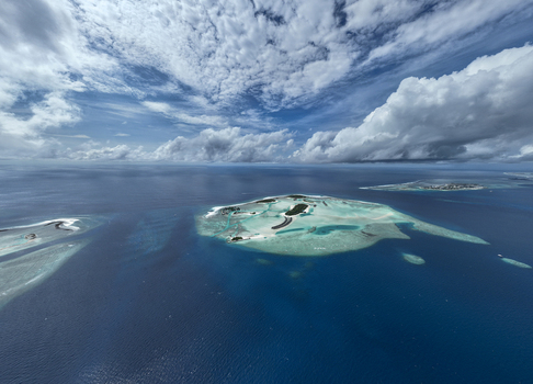 Aerial view of a tropical island surrounded by turquoise lagoon waters and deep blue ocean under a dramatic cloudy sky in the Maldives. Aerial view of a tropical island surrounded by turquoise lagoon waters and deep blue ocean under a dramatic cloudy sky in the Maldives.