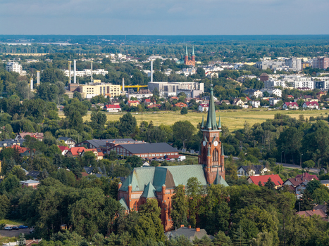 Aerial view of the Church of St. Casimir surrounded by lush green trees residential houses and industrial buildings in the background in Pruszkow Masovian Voivodeship Poland. Aerial view of the Church of St. Casimir surrounded by lush green trees residential houses and industrial buildings in the background in Pruszkow Masovian Voivodeship Poland.