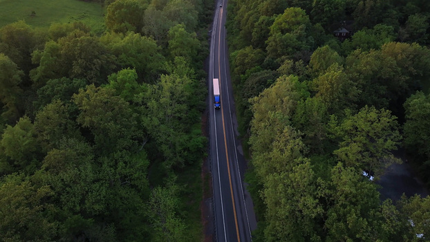 Aerial view of a truck driving along a winding road surrounded by dense green forest in Elizabeth Township Pennsylvania United States.