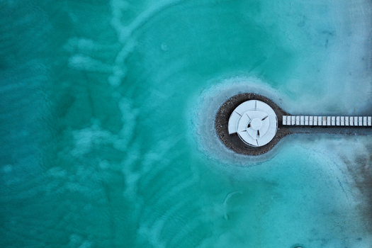 Aerial view of a stark white geometric structure on a circular island connected by a pier amidst swirling turquoise and teal water Ein Bokek Israel. Aerial view of a stark white geometric structure on a circular island connected by a pier amidst swirling turquoise and teal water Ein Bokek Israel.