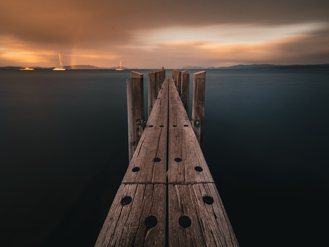 View of a wooden jetty extending into the calm waters of the bay at sunset with a faint rainbow visible in the distance in Little Grove Western Australia Australia. View of a wooden jetty extending into the calm waters of the bay at sunset with a faint rainbow visible in the distance in Little Grove Western Australia Australia.