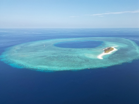 Aerial view of Pulau Ndaa a small tropical island surrounded by a vibrant coral reef and turquoise lagoon in the middle of the deep blue sea. Tomia South East Sulawesi Indonesia.