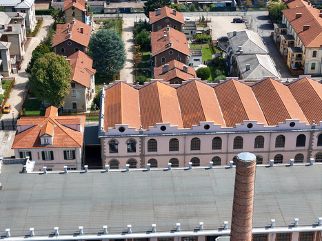 Aerial view of Villaggio Leumann featuring the historic factory with sawtooth roofs and a brick chimney among residential houses in Collegno Piemonte Italy. Aerial view of Villaggio Leumann featuring the historic factory with sawtooth roofs and a brick chimney among residential houses in Collegno Piemonte Italy.