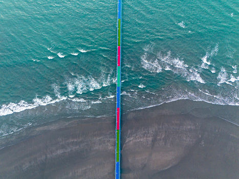 Aerial view of a colorful bridge stretching over the turquoise sea with waves crashing against the dark sandy shore Cox s Bazar Chittagong Division Bangladesh.