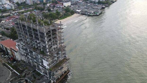 Aerial view of an abandoned concrete building structure on the coastline with surrounding urban rooftops and calm sea water in Balikpapan East Kalimantan Indonesia. Aerial view of an abandoned concrete building structure on the coastline with surrounding urban rooftops and calm sea water in Balikpapan East Kalimantan Indonesia.