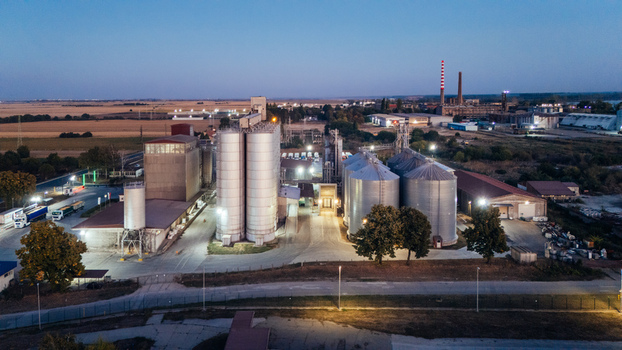 Aerial view of an industrial grain silo facility illuminated at dusk with surrounding fields and infrastructure in Sremska Mitrovica Vojvodina Serbia. Aerial view of an industrial grain silo facility illuminated at dusk with surrounding fields and infrastructure in Sremska Mitrovica Vojvodina Serbia.