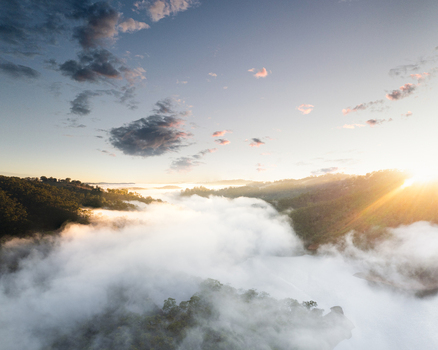Aerial view of Kangaroo Creek Reservoir covered by thick morning fog and low clouds with golden sunrise light over forested hills in Adelaide Hills Council South Australia Australia. Aerial view of Kangaroo Creek Reservoir covered by thick morning fog and low clouds with golden sunrise light over forested hills in Adelaide Hills Council South Australia Australia.