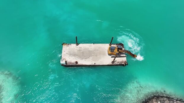 Aerial view of an excavator on a barge in turquoise waters Maldives. Aerial view of an excavator on a barge in turquoise waters Maldives.