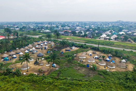 Aerial view of a rural settlement with numerous traditional round huts with thatched roofs surrounded by lush green vegetation and palm trees near a road in Port Harcourt Rivers State Nigeria. Aerial view of a rural settlement with numerous traditional round huts with thatched roofs surrounded by lush green vegetation and palm trees near a road in Port Harcourt Rivers State Nigeria.