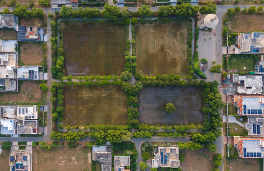Aerial view of a residential neighborhood with a central park divided into four sections by tree lined paths houses with solar panels and a water tower in Lahore Punjab Pakistan.