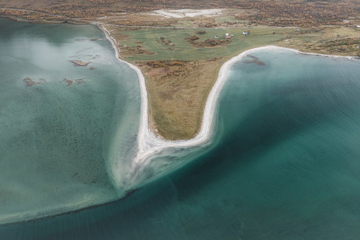 Aerial view of the Lofoten coastline featuring a narrow sandy spit extending into the turquoise sea surrounded by green fields and small houses in Svolvaer Nordland Norway.