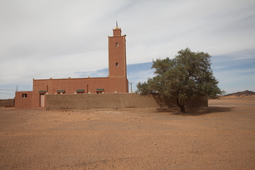 View of a traditional earthen mosque with a minaret standing in the arid desert landscape of Morocco.