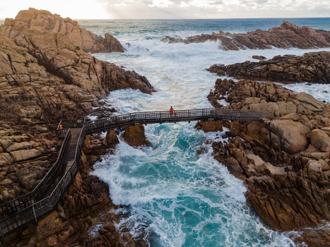 Aerial view of Canal Rocks Bridge with a person standing on the wooden walkway surrounded by rugged granite rocks and crashing turquoise waves in Yallingup Western Australia Australia. Aerial view of Canal Rocks Bridge with a person standing on the wooden walkway surrounded by rugged granite rocks and crashing turquoise waves in Yallingup Western Australia Australia.