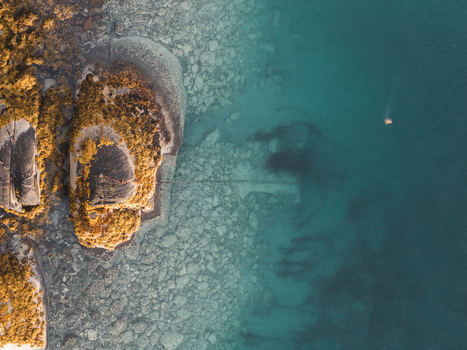 Aerial view of the rocky coastline of Lofoten with clear turquoise water seaweed covered rocks and a small boat in the sea Svolvaer Nordland Norway.