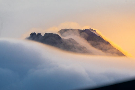 View of a rugged mountain peak rising above a thick layer of clouds during golden hour in Costa Rica.