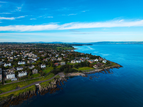 Aerial view of Bangor Harbour and Town with coastal houses green lawns rocky shoreline and blue sea under a clear sky in Bangor Northern Ireland United Kingdom.