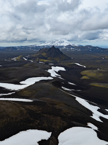 Aerial view of Krakatindur mountain surrounded by dark volcanic soil patches of snow and rugged terrain in Rangarthing ytra Iceland. Aerial view of Krakatindur mountain surrounded by dark volcanic soil patches of snow and rugged terrain in Rangarthing ytra Iceland.