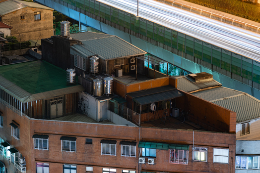 View of a brick apartment building at night with rooftop water tanks and laundry featuring light trails from a nearby highway in Sanchong District New Taipei City Taiwan. View of a brick apartment building at night with rooftop water tanks and laundry featuring light trails from a nearby highway in Sanchong District New Taipei City Taiwan.