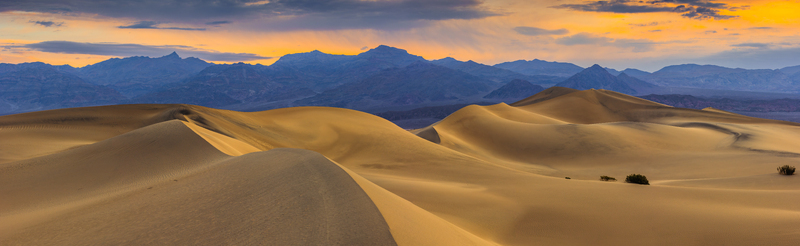 View of the sand dunes at Death Valley National Park under a golden sunset sky with distant mountains in the background United States.