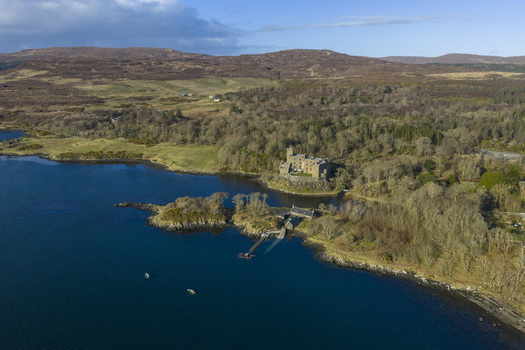 Aerial view of Dunvegan Castle and Gardens on the shore of Loch Dunvegan surrounded by lush woodlands and rolling hills Isle of Skye Scotland United Kingdom. Aerial view of Dunvegan Castle and Gardens on the shore of Loch Dunvegan surrounded by lush woodlands and rolling hills Isle of Skye Scotland United Kingdom.