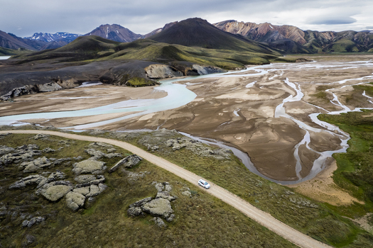 Aerial view of a white vehicle driving on the F208 road through the volcanic landscape and braided rivers of the Icelandic Highlands Iceland. Aerial view of a white vehicle driving on the F208 road through the volcanic landscape and braided rivers of the Icelandic Highlands Iceland.