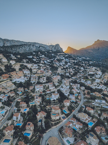 Aerial view of a hillside residential area with winding roads swimming pools and Mediterranean architecture nestled against the mountains at sunset in Calp Valencian Community Spain. Aerial view of a hillside residential area with winding roads swimming pools and Mediterranean architecture nestled against the mountains at sunset in Calp Valencian Community Spain.