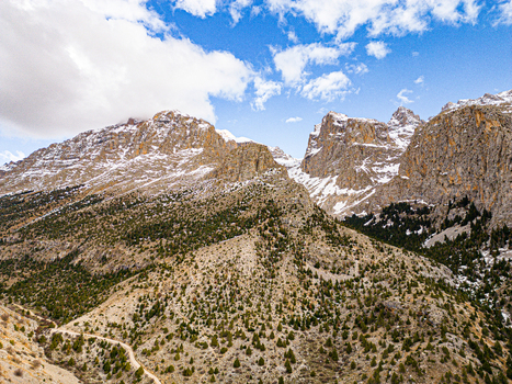 Aerial view of Aladaglar National Park featuring rugged snow capped mountain peaks rocky slopes scattered evergreen trees and a winding dirt path in Demirkazik Nigde Turkiye. Aerial view of Aladaglar National Park featuring rugged snow capped mountain peaks rocky slopes scattered evergreen trees and a winding dirt path in Demirkazik Nigde Turkiye.