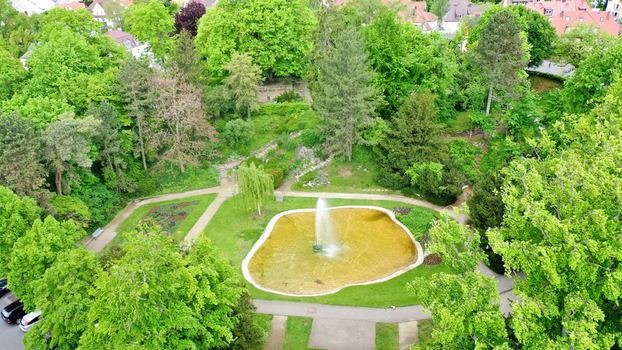 Aerial view of Stadtpark featuring a central fountain and pond surrounded by lush green trees and winding walking paths in Forchheim Bayern Germany. Aerial view of Stadtpark featuring a central fountain and pond surrounded by lush green trees and winding walking paths in Forchheim Bayern Germany.