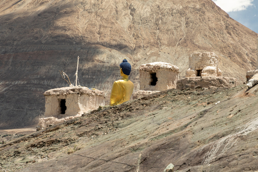 View of the golden Buddha statue at Charasa Gonpa surrounded by ancient stone stupas and rugged mountain terrain in Charasa Ladakh India.