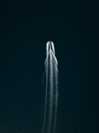 Aerial view of a motorboat cruising through deep blue water leaving a long white wake behind Augusta Sicily Italy. Aerial view of a motorboat cruising through deep blue water leaving a long white wake behind Augusta Sicily Italy.