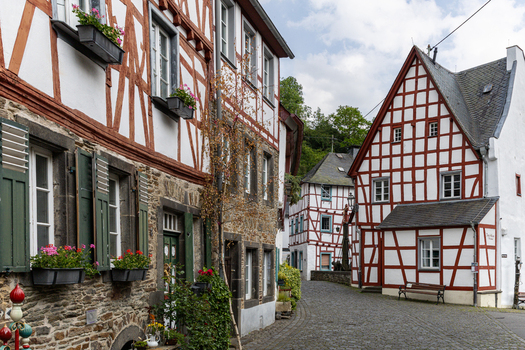 View of traditional half timbered houses with red frames and flower boxes along a narrow cobblestone street in the historic village of Monreal Rhineland Palatinate Germany. View of traditional half timbered houses with red frames and flower boxes along a narrow cobblestone street in the historic village of Monreal Rhineland Palatinate Germany.