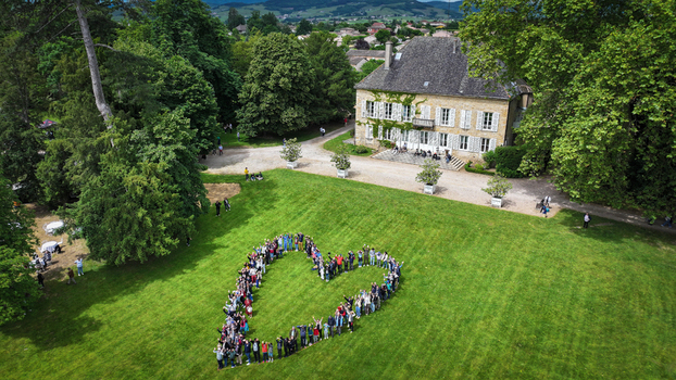 La Chapelle de Guinchay France 01 June 2024 Aerial view of a large group of people forming a heart shape on a green lawn in front of a historic stone manor house.