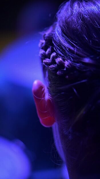View of a young woman s braided hairstyle under blue stage lighting.