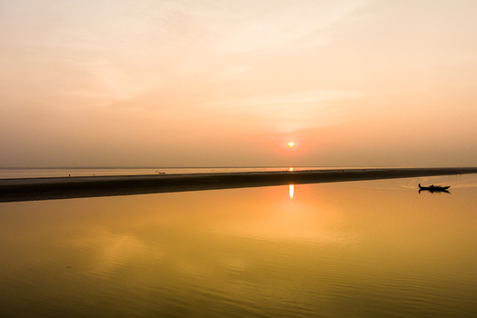 Aerial view of the Padma River at sunset with a small boat gliding across the calm golden water in Rajshahi Rajshahi Division Bangladesh.