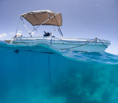View of a small motorboat with a canopy floating on crystal clear turquoise water under a bright blue sky in Guanaja Bay Islands Department Honduras. View of a small motorboat with a canopy floating on crystal clear turquoise water under a bright blue sky in Guanaja Bay Islands Department Honduras.
