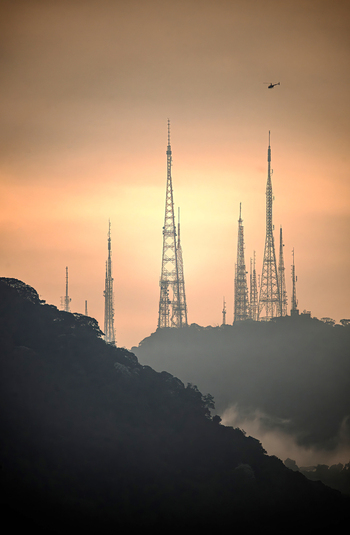 View of silhouetted telecommunication towers on a misty hill with a helicopter in the sky during sunset Rio de Janeiro State of Rio de Janeiro Brazil. View of silhouetted telecommunication towers on a misty hill with a helicopter in the sky during sunset Rio de Janeiro State of Rio de Janeiro Brazil.