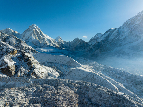 Aerial view of snow capped Himalayan peaks with rugged rocky slopes deep glacial valleys and clear blue sky in Nepal.