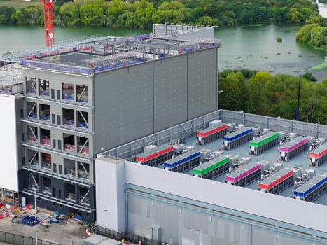 Aerial view of a large data center under construction featuring rooftop cooling units and a crane near a river in the United Kingdom.