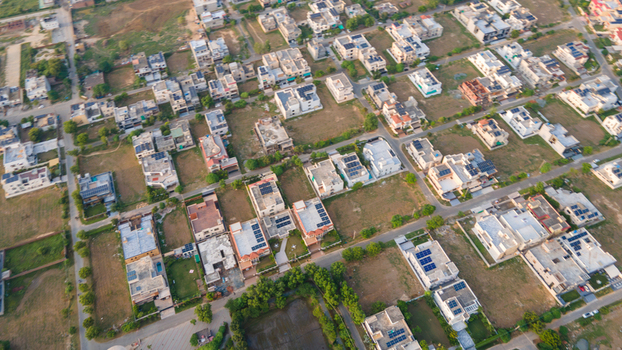 Aerial view of a residential neighborhood featuring houses with flat roofs some with solar panels interspersed with empty plots and roads in Lahore Punjab Pakistan.