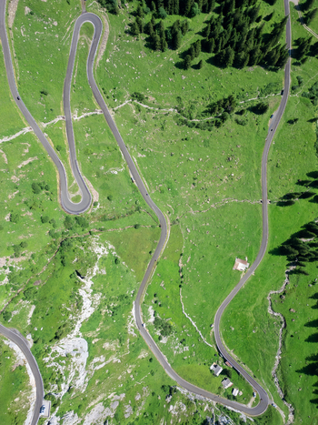 Aerial view of a serpentine road winding through verdant meadows and dark green forests a contrast of man made curves against nature s soft textures Spiringen Uri Switzerland. Aerial view of a serpentine road winding through verdant meadows and dark green forests a contrast of man made curves against nature s soft textures Spiringen Uri Switzerland.