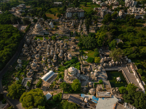 Aerial view of Ahar Cenotaphs with numerous white marble domes and chhatris surrounded by lush green trees and a small water tank in Udaipur Rajasthan India.
