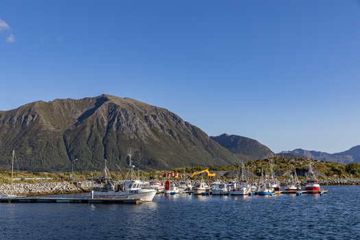 View of fishing boats docked in the Laukvik harbor with rugged mountains in the background under a clear blue sky Laukvik Nordland Norway. View of fishing boats docked in the Laukvik harbor with rugged mountains in the background under a clear blue sky Laukvik Nordland Norway.