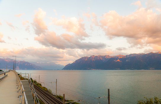 View of the railway tracks running along the shore of Lake Geneva at sunset with mountains in the background in Bourg en Lavaux Vaud Switzerland. View of the railway tracks running along the shore of Lake Geneva at sunset with mountains in the background in Bourg en Lavaux Vaud Switzerland.
